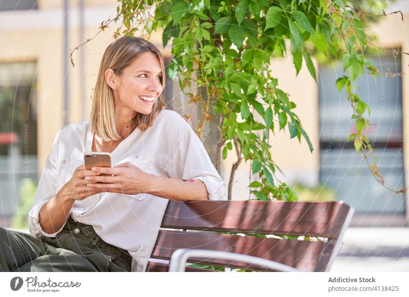Stylish woman with mobile phone chilling on bench in summer day smartphone lifestyle using texting modern rest device gadget connection communicate online