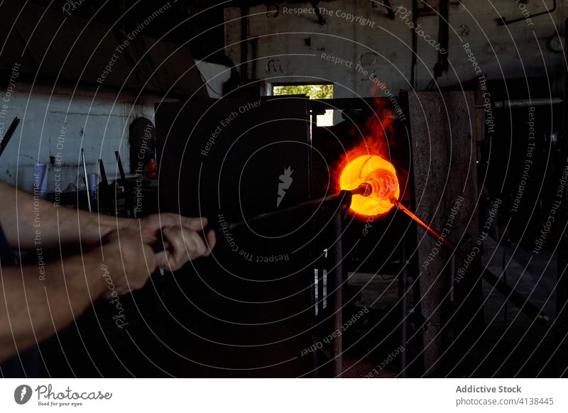 Glass blower melting glass in furnace man blowpipe workshop hot craft equipment craftsman skill industry production manufacture small business flame