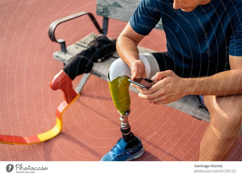 Disabled athlete using phone man runner unrecognized faceless sport prosthesis prosthetic disability disabled amputation amputee anonymous type typing