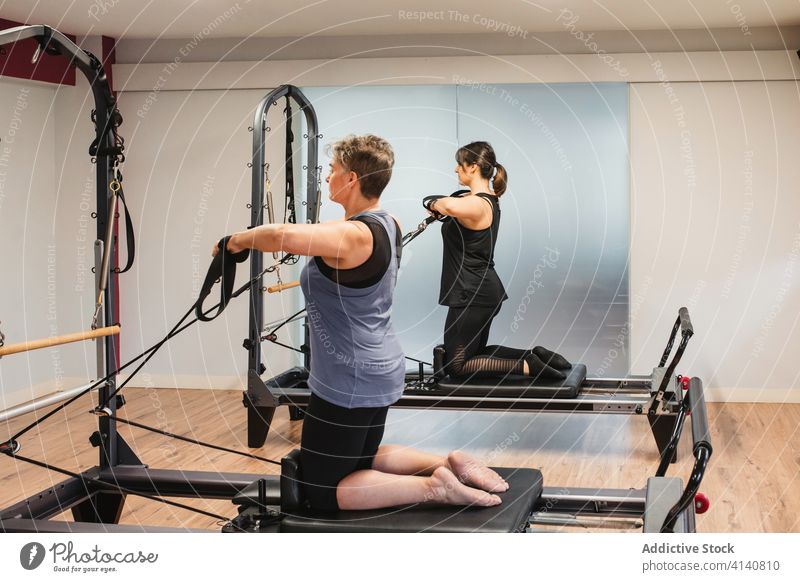 Side view of fit woman doing legs exercise with resistance ropes on Pilates  reformer in gym