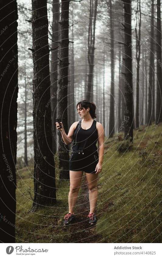 Female runner listening to music in misty wood woman smartphone tired break using training forest female woods fog narrow activewear sportswoman path healthy