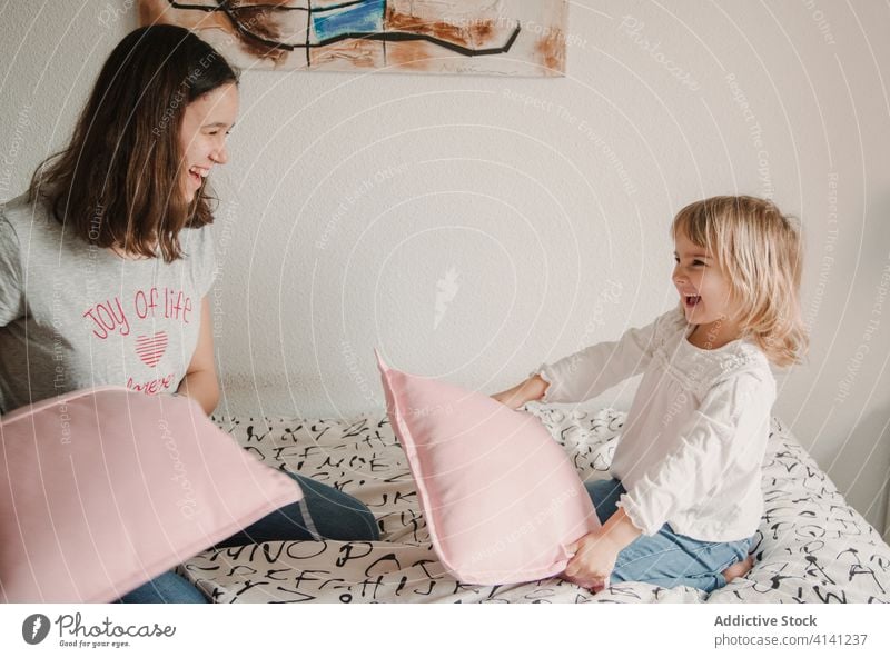 Delighted sisters fighting with pillows on bed playful having fun game girl sibling little teenage cozy together happy childhood home bedroom joy laugh kid