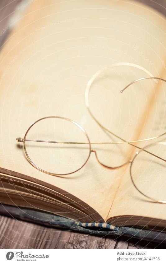 Opened book with eyeglasses on table open antique old fashioned wooden retro shabby vintage desk creative library collection textbook story paper education