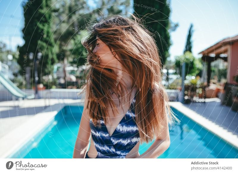 Content woman in swimsuit at poolside flying hair summer vacation carefree swimwear content female sunny relax rest holiday cheerful joy resort water smile