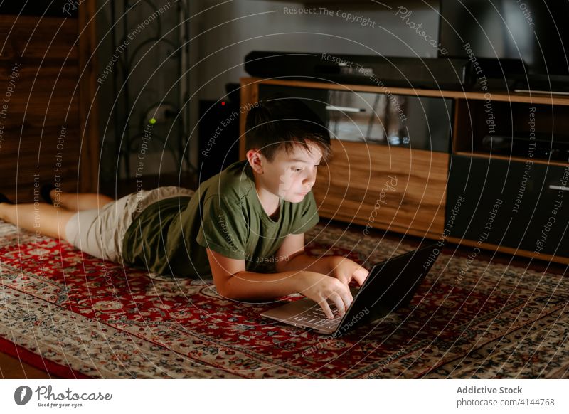 Thoughtful child watching cartoon on netbook at home boy laptop lying floor pensive movie device internet gadget online using weekend kid little casual relax