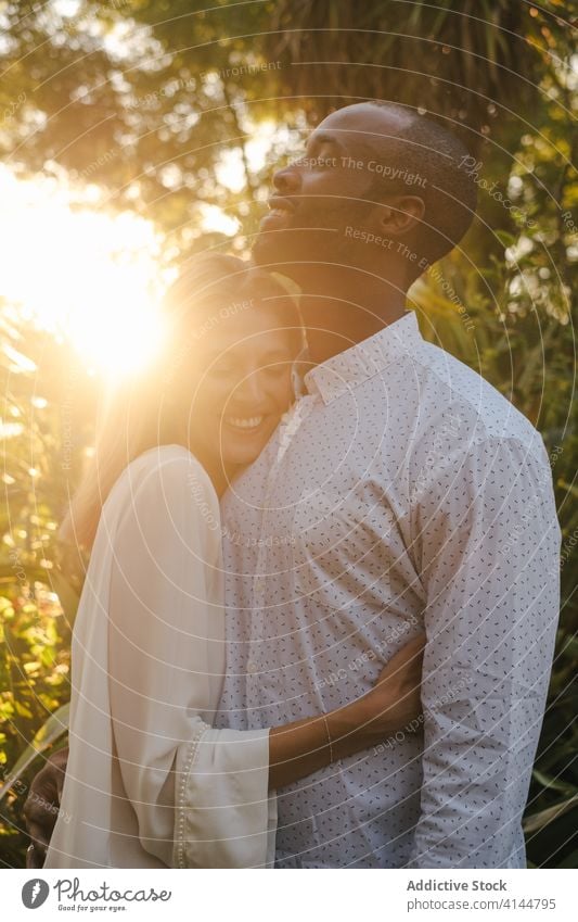 Romantic diverse couple hugging passionately in the evening garden tender romantic content eyes closed sunset love affection embrace bonding modern casual
