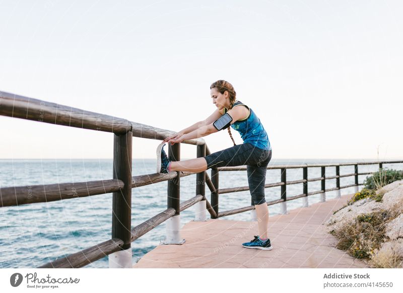 Slim woman stretching during training on seafront warm up waterfront slim athlete workout confident female armband promenade sportswear fitness activity