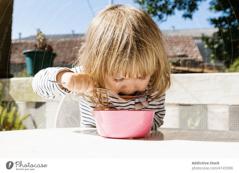 Charming girl sitting at table during breakfast adorable child morning terrace smile food bowl kid happy relax sunny summer courtyard backyard little healthy