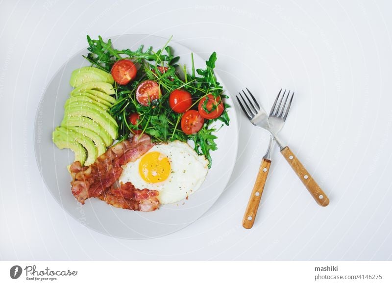 tasty breakfast - fried egg and bacon served with arugula tomato salad and fresh avocado on white plate food meal morning vegetable brunch organic