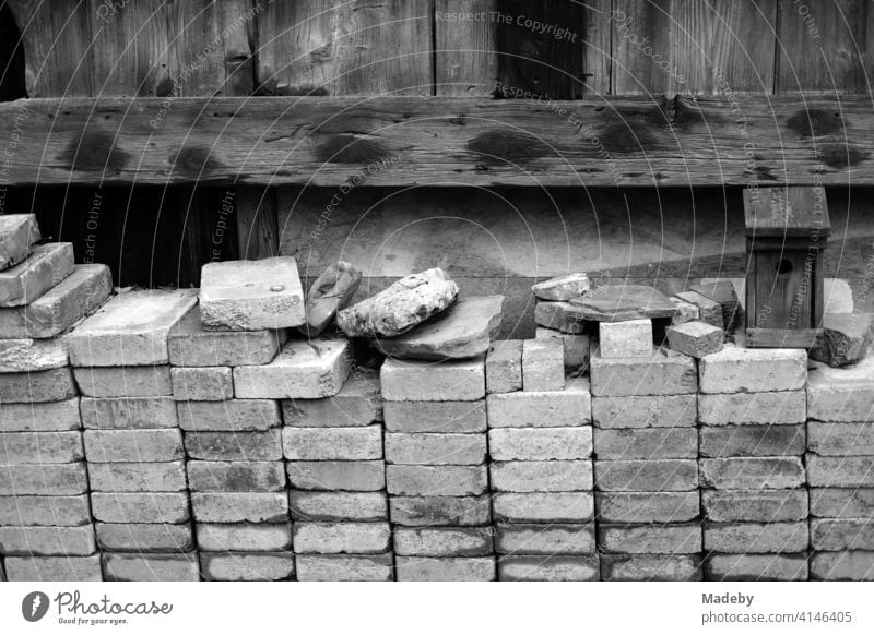 Carefully and neatly stacked bricks in front of an old wooden barn on a farm in Rudersau near Rottenbuch in the district of Weilheim-Schongau in Upper Bavaria, photographed in classic black and white