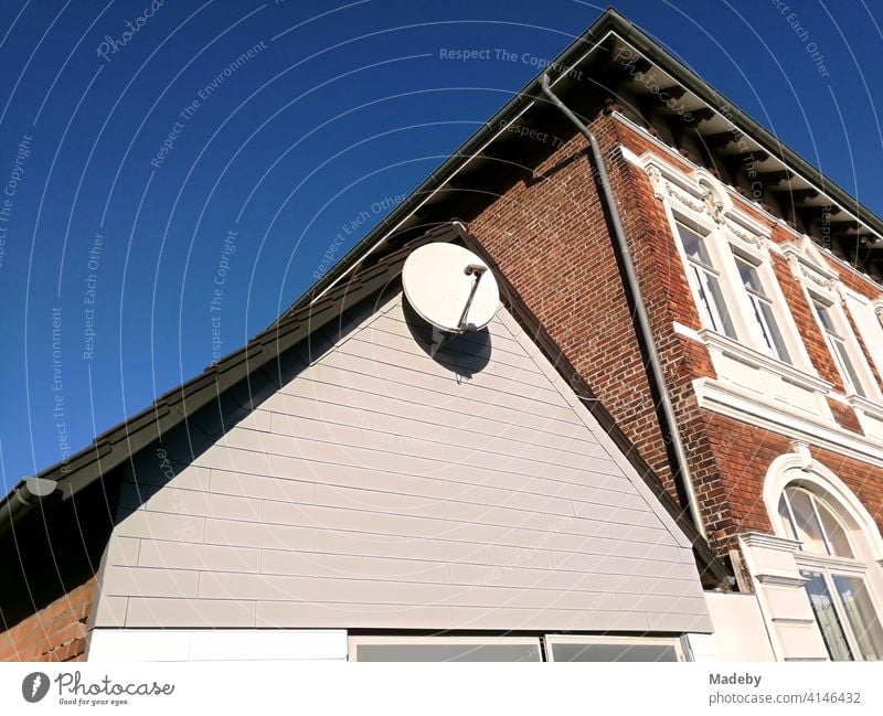 Satellitenschüsel im Spitzgiebel eines Nebengebäude vor einem schönen Altbau im Sonnenschein in Lemgo bei Detmold in Ostwestfalen-Lippe Satellitenschüssel