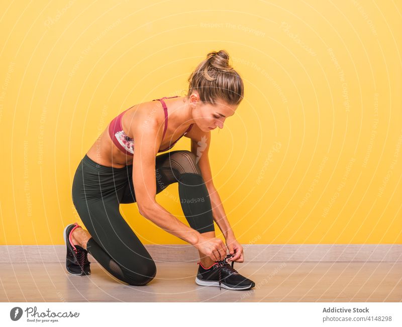 Fit woman tying shoelaces in gym tie sportswoman training sneakers leggings confident fitness female modern workout slim bra healthy sportswear athlete body
