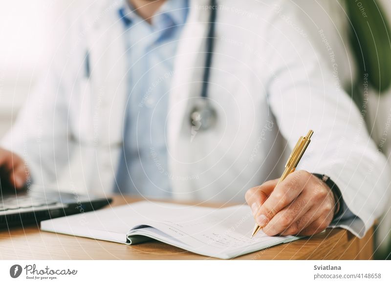 A young doctor of oriental appearance works while sitting at the table in the network with a laptop and makes notes in a notebook medicine person health clinic