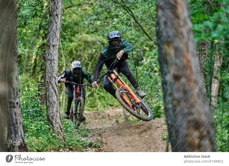 Professional cyclists showing tricks on bikes downhill stunt men ride bicycle together extreme perform risk helmet professional road forest woods above ground