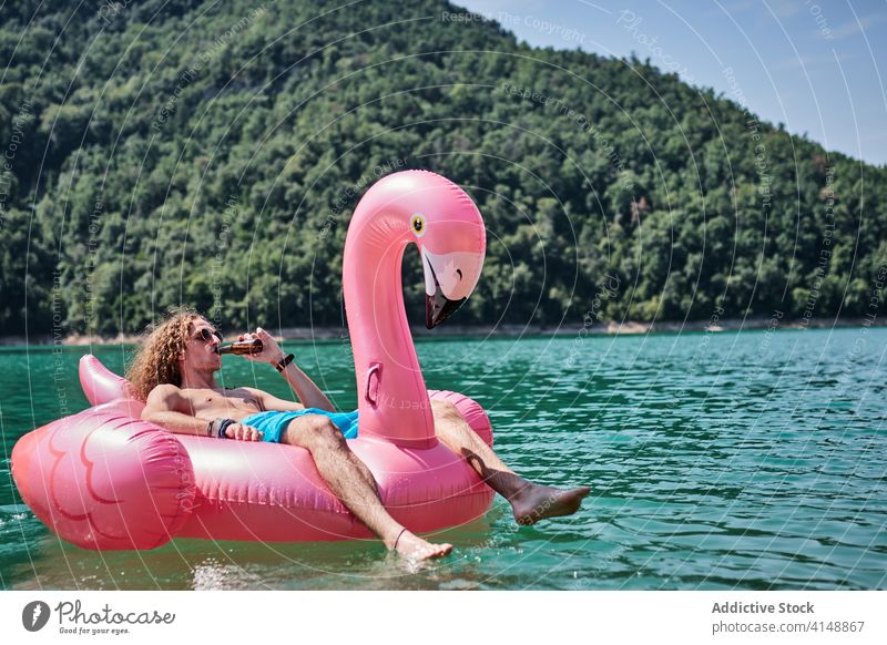 Man in inflatable ring on lake man relax float drink alcohol flamingo shape male lying bottle water holiday recreation summer vacation rest beverage nature