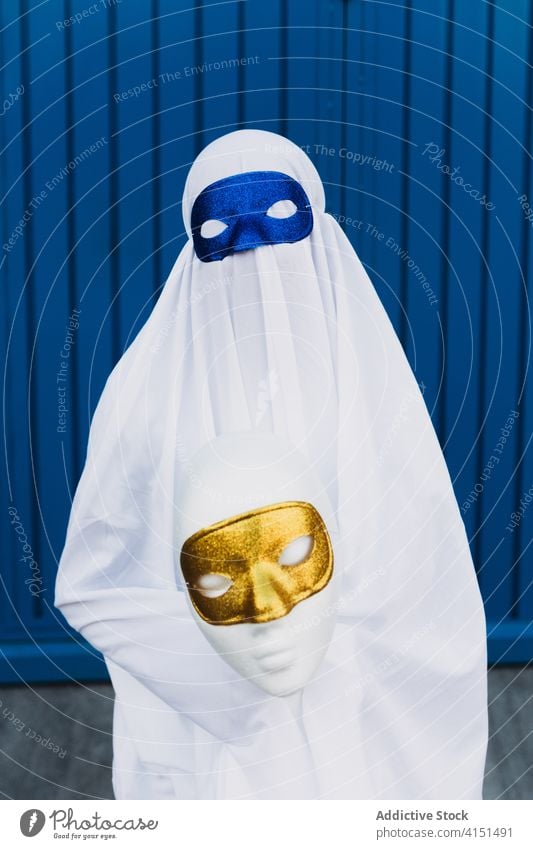 Anonymous child in ghost costume on street halloween mask masquerade kid holiday event autumn city building urban suit scary entertain spooky celebrate season