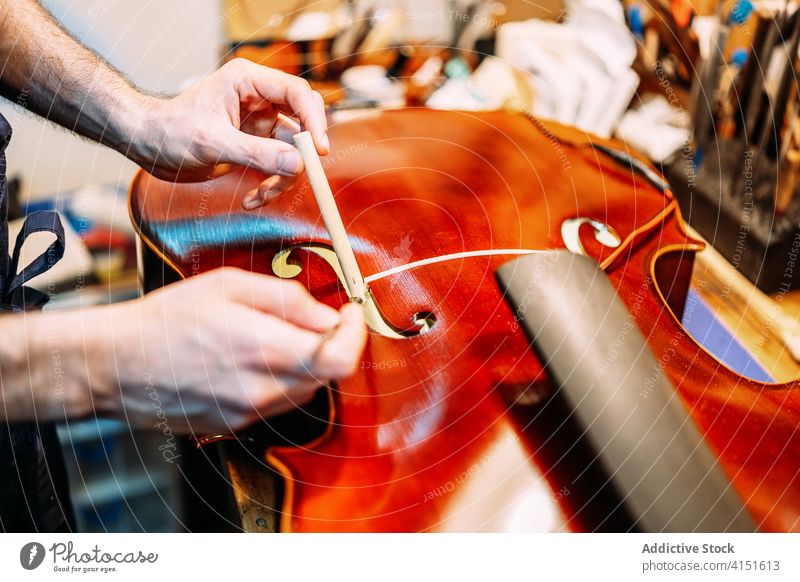 Anonymous luthier installing sound post to violin insert make instrument artisan craft tool hand work setting workshop equipment cello skill master maker