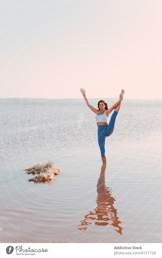 Full length of a slim woman practicing yoga standing on a mat by ocean  stock photo