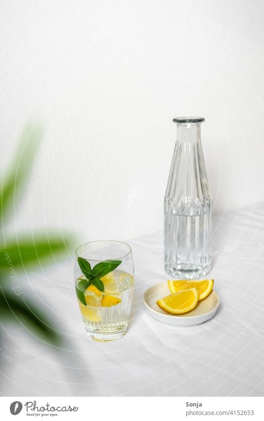 A water bottle and a drinking glass with water, lemon and peppermint on a white tablecloth Water Lemon Peppermint Cold drink Refreshment Fresh Lemonade Yellow