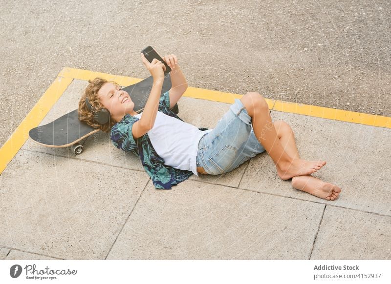 Smiling boy lying on the floor with a skateboard listening to music on his mobile loud adolescence solitude singing trend generation teen weekend sound teenager