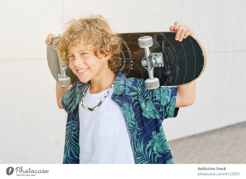 Portrait of a boy carrying a skateboard on his back while smiling adolescence vitality independence teen fashionable teenager youth posing balance hipster shirt