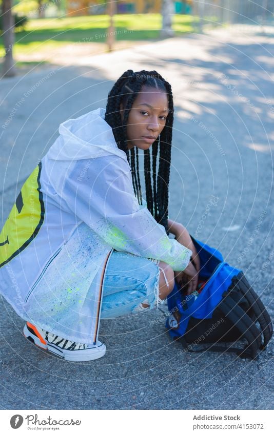 Young black woman with bag sitting in park fashion style denim trendy young hipster braid urban street style ethnic african american millennial female jeans
