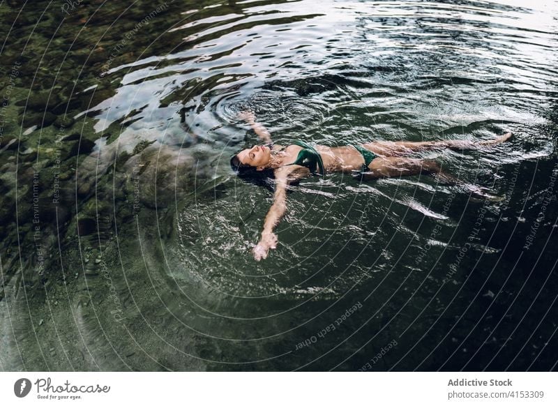 Serene woman floating on lake water swim enjoy vacation serene relax pond bikini female summer lying eyes closed swimwear rest recreation slim nature lady