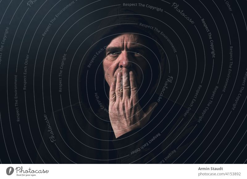 portrait of a man with a hoodie holding a hand in front of his mouth angle banned beard black blur breath casual caucasian close-up closeup confident cool