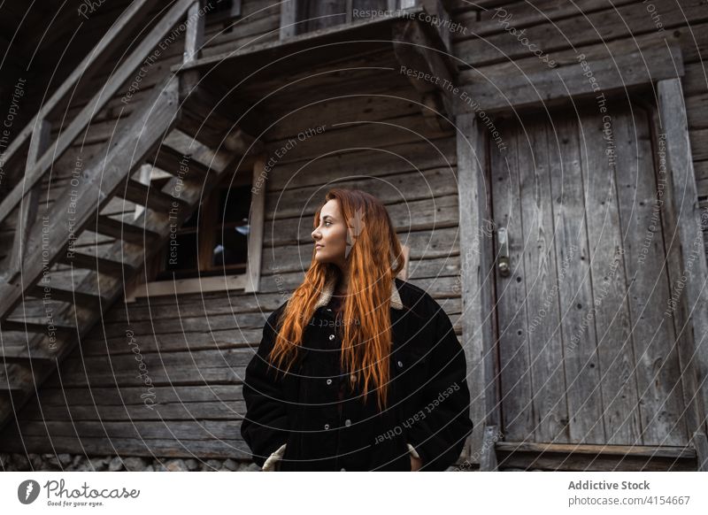 Young woman standing near weathered wooden cabin building aged house countryside door ladder young female tourist lumber timber shabby exterior old journey