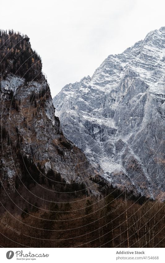 Rough rocky mountain slope covered with snow and forest rough ridge cold overcast gloomy majestic nature landscape gray autumn weather season range environment