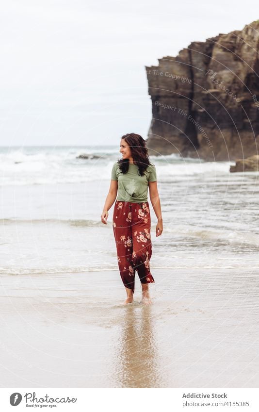 Smiling woman on beach in summer wet seashore walk water cliff seaside female relax travel tourism traveler coast ocean rocky nature happy vacation lady holiday