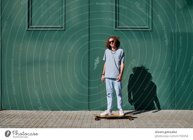 a young man with curly hair skating outdoors with a green wall behind him longboard che skateboard attractive person skateboarding sport skater male guy casual