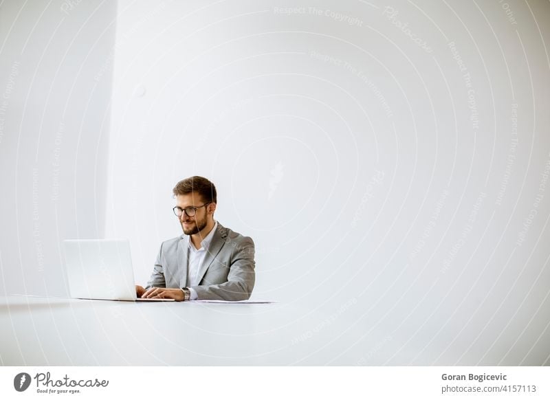 Young man working on laptop in bright office adult attractive beautiful behind business caucasian communication computer confident day desk elegant employee
