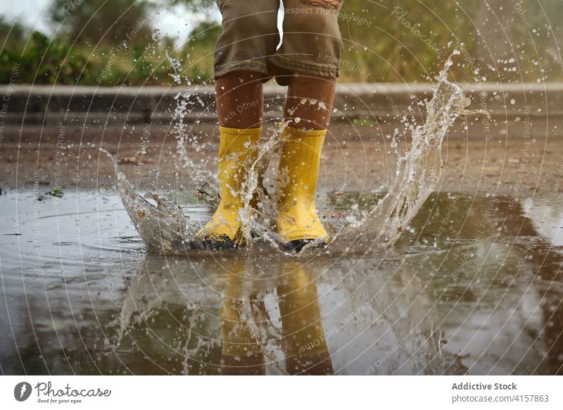 Detail of yellow rain boots hitting a puddle splashing water in a path joke innocence lifestyles messy jump playful kids enjoyment wet weather drop reflection