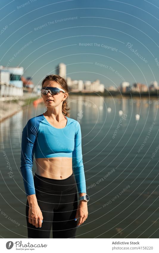 Slim active woman in sportswear and sunglasses standing near river sporty confident fit slim training fitness workout tracker smart watch embankment female