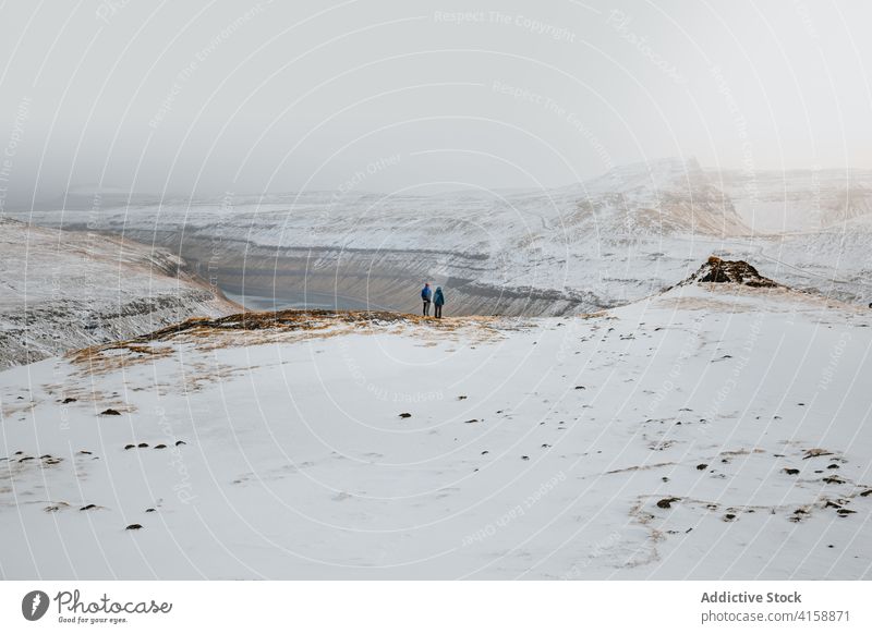 Anonymous people contemplating amazing view of mountains river snow winter landscape cloudy season cold range faroe islands overcast sky ridge nature rock shore