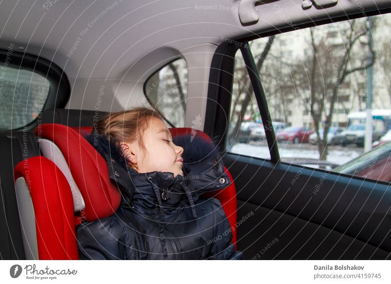 girl in blue warm clothes sits unbuckled in a car seat and sleeps daughter comfortable back door red window safely defence secure passenger inside hat vehicle