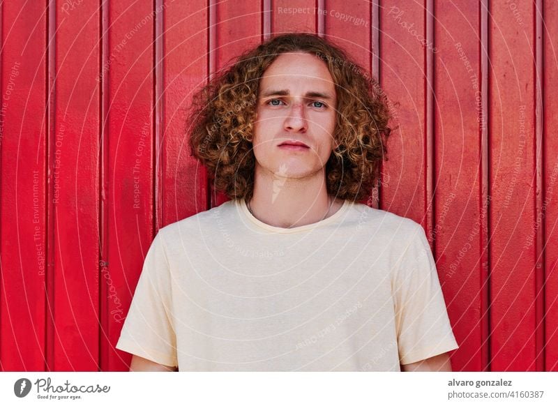 portrait of a serious young man with curly hair and green eyes looking at camera with a red background che attractive person male guy casual white handsome one
