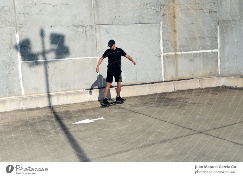 Teenager dressed in black and cap skateboarding in industrial zone teenager parking lot abandoned layered haircut solo rooftop seriousness clear sky shorts
