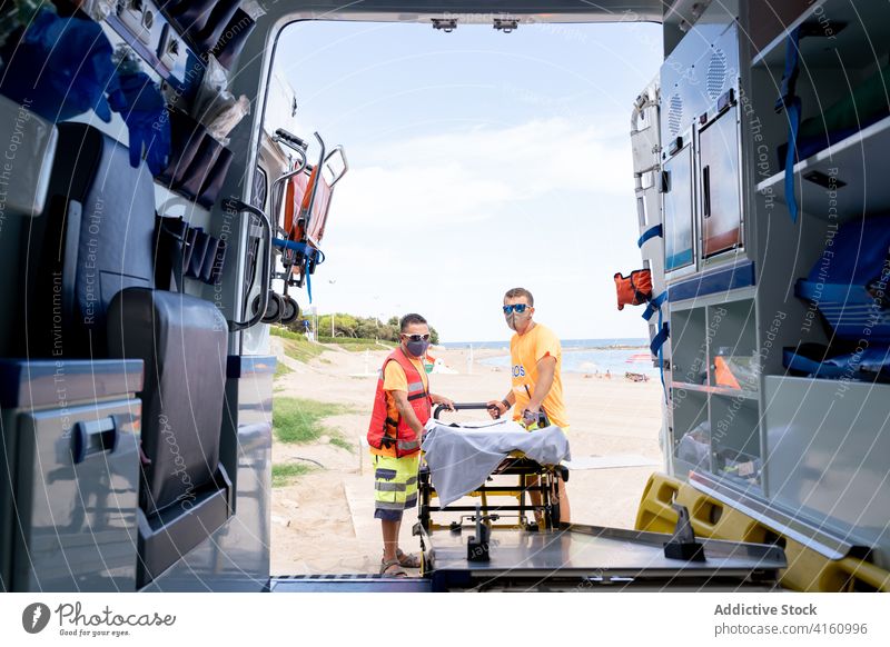 Anonymous lifeguards with stretcher near ambulance car on street colleague uniform helmet practice training men service medical gurney vehicle work professional