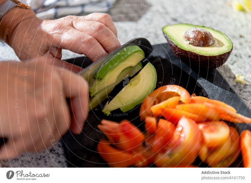 Crop mature woman cutting avocado on board tomato vegetable cook culinary food process gastronomy recipe kitchen cuisine contemporary dinner chef prepare