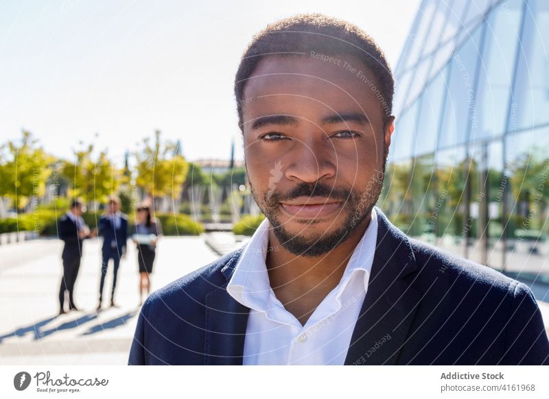 Smiling young black businessman standing on street near glass building entrepreneur happy smile elegant well dressed classy handsome colleague contemporary male