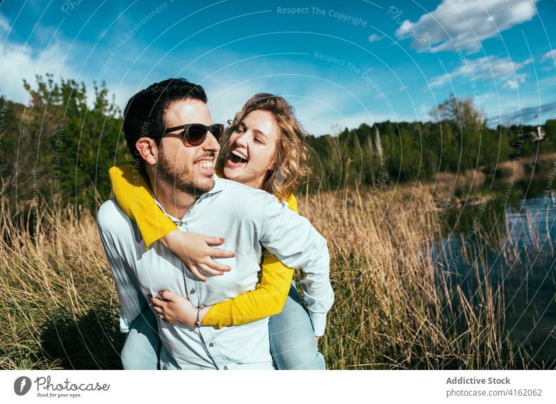 Happy couple having fun together near lake piggyback cheerful hug love freedom carefree girlfriend boyfriend sunglasses weekend handsome relax relationship
