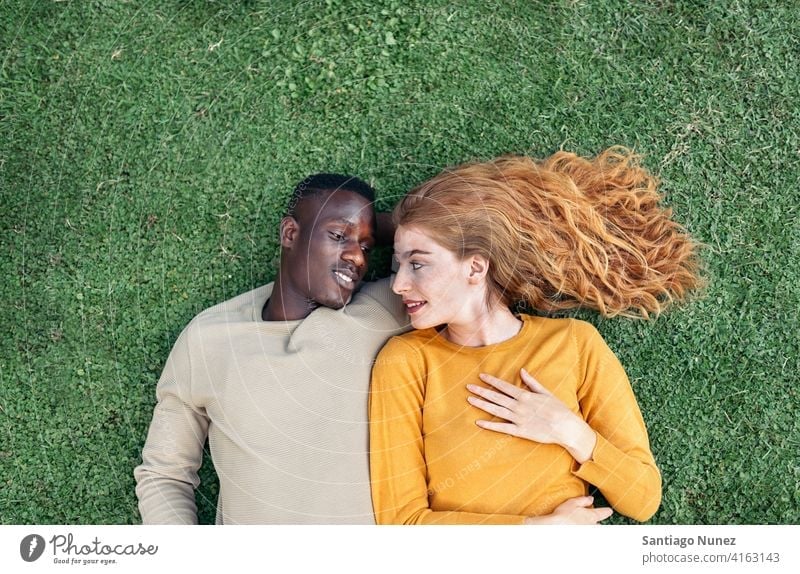 Multiethnic Couple Cuddling in the Grass lying grass looking at each other top view portrait relationship multi-racial black man caucasian multi-cultural