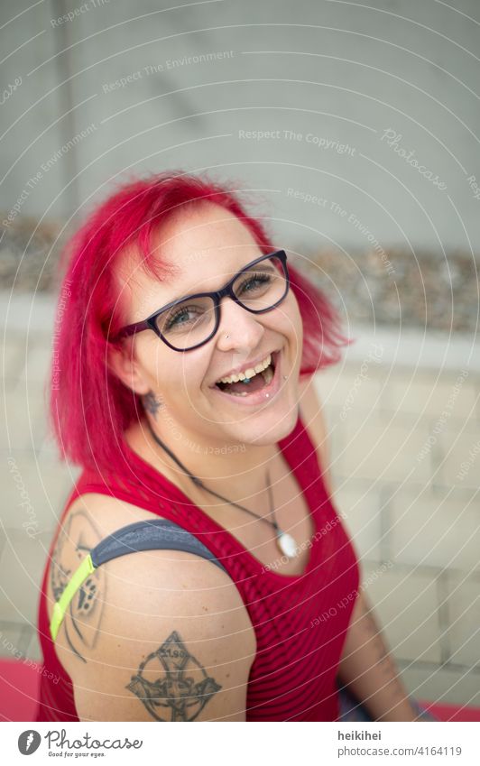 A young redhead woman with glasses and tattoos looks at the camera laughing Woman Eyeglasses Red-haired portrait Lip piercing conspicuous appearance Emanation