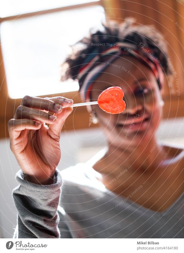 Young black woman at home smiling with a lollipop in her hand beauty african-american people lady model expression hairstyle indoor indoors laughing joy smile
