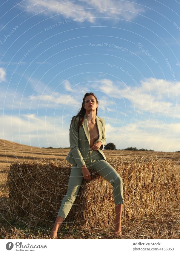 Fashionable young woman resting on haystack in countryside confident style fashion sensual naked nature model tranquil female slim suit barefoot body bale