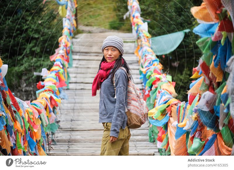 Ethnic female traveler on suspension bridge decorated with piece of fabric woman bright tourism warm clothes wanderlust trip explore discover ethnic wooden hat