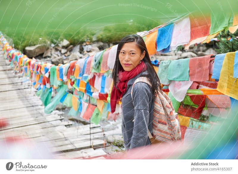 Ethnic female traveler on suspension bridge decorated with piece of fabric woman bright tourism warm clothes wanderlust trip explore discover ethnic wooden hat