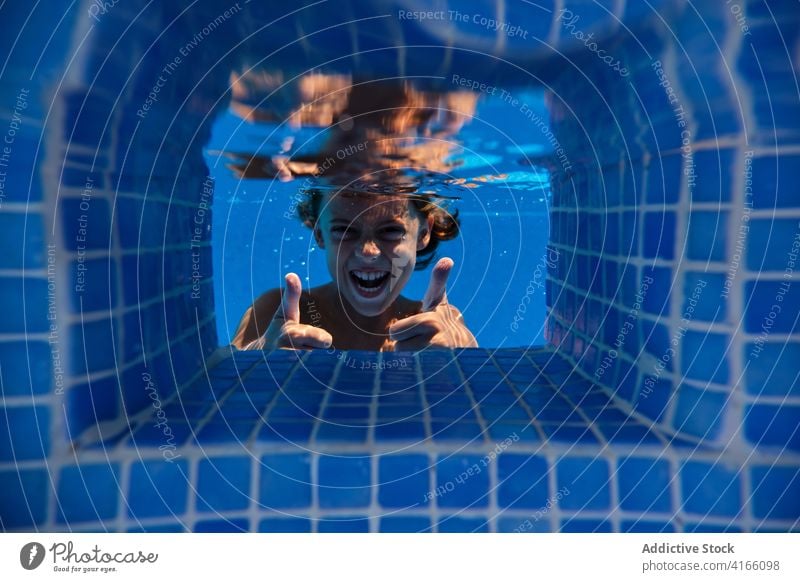 Excited boy showing thumbs up through pool water excited thumb up gesture having fun carefree cheerful underwater activity smile playful splash aqua active